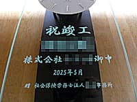 「祝竣工、贈り先の会社名、竣工日の日付、贈り主の会社名」を前面ガラスに彫刻した、新社屋竣工祝い用の壁掛け時計