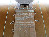 お祝いメッセージ、保育園の名前、日付、贈り主の名前、音符マークのイラストを彫刻した保育園の開園祝い用の名入れ掛け時計